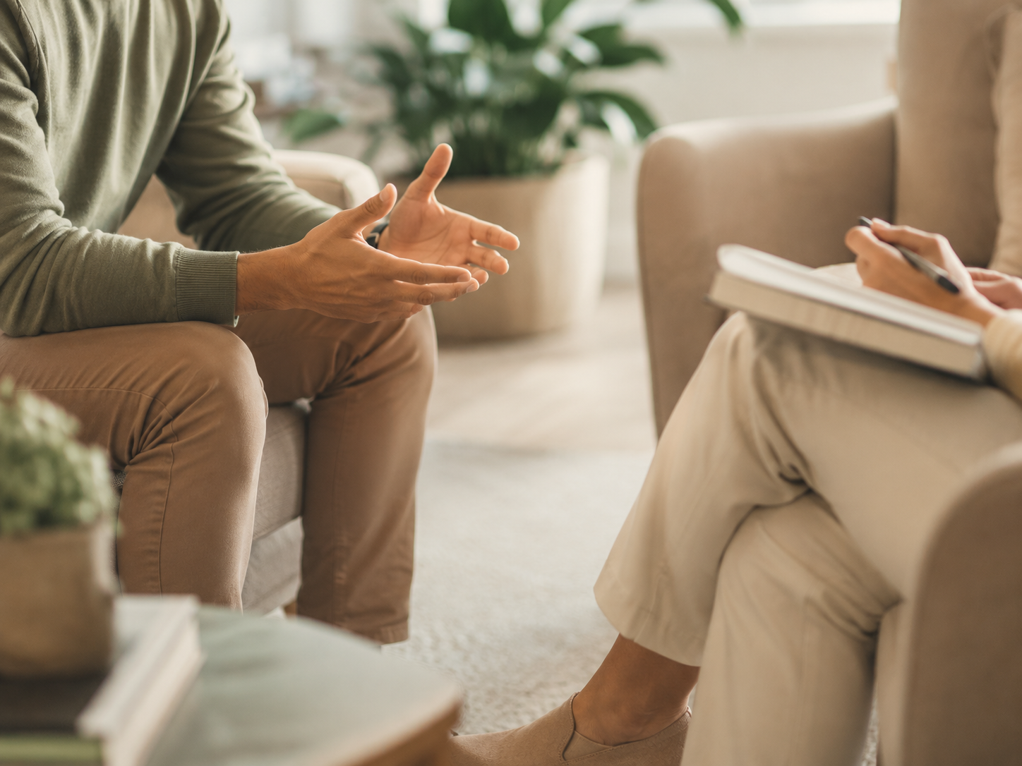 Two people seated in a calm coaching session, one gesturing expressively while the other takes notes